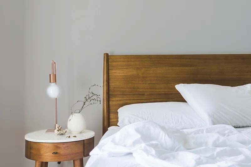 A bed with white sheets and pillows next to a nightstand with a lamp on it.