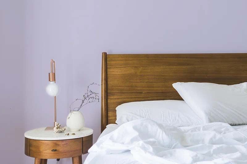 A bedroom with a bed , nightstand , lamp and purple walls.
