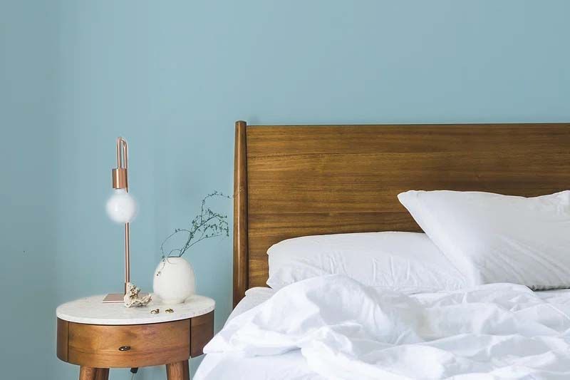 A bed with white sheets and pillows next to a nightstand and a lamp.