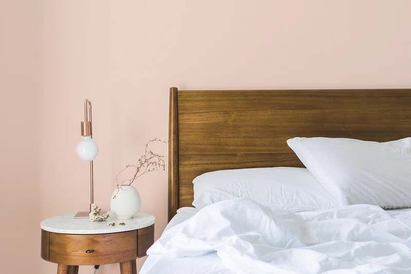 A bedroom with a bed , nightstand , lamp and pink walls.