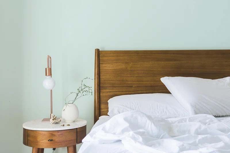 A bed with white sheets and pillows next to a nightstand and a lamp.