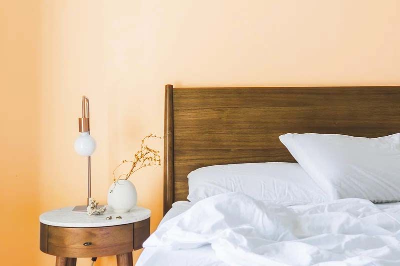 A bed with white sheets and pillows next to a nightstand with a lamp on it.