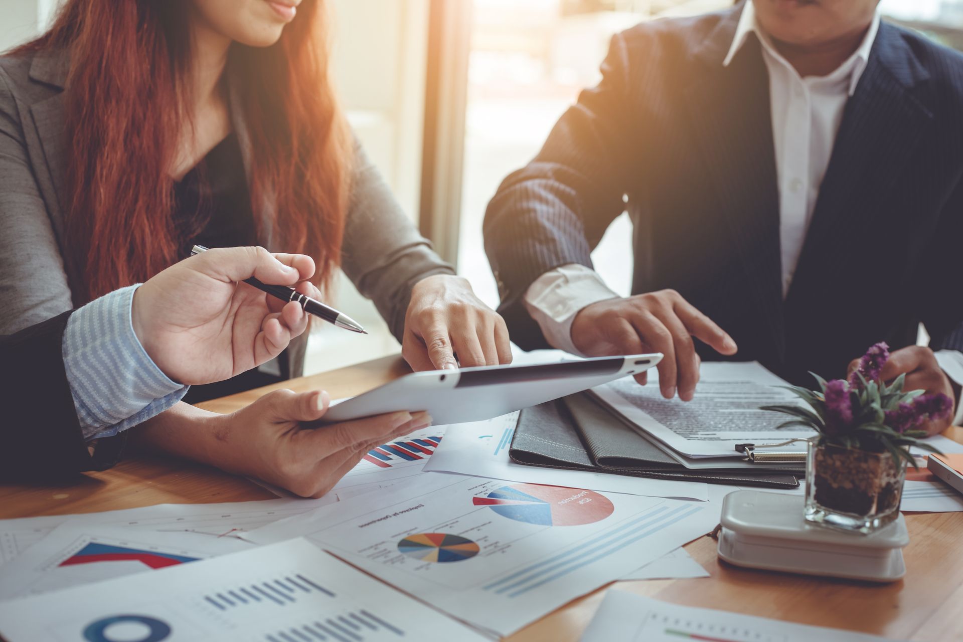 Two people reviewing financial documents, discussing data analysis at a desk.