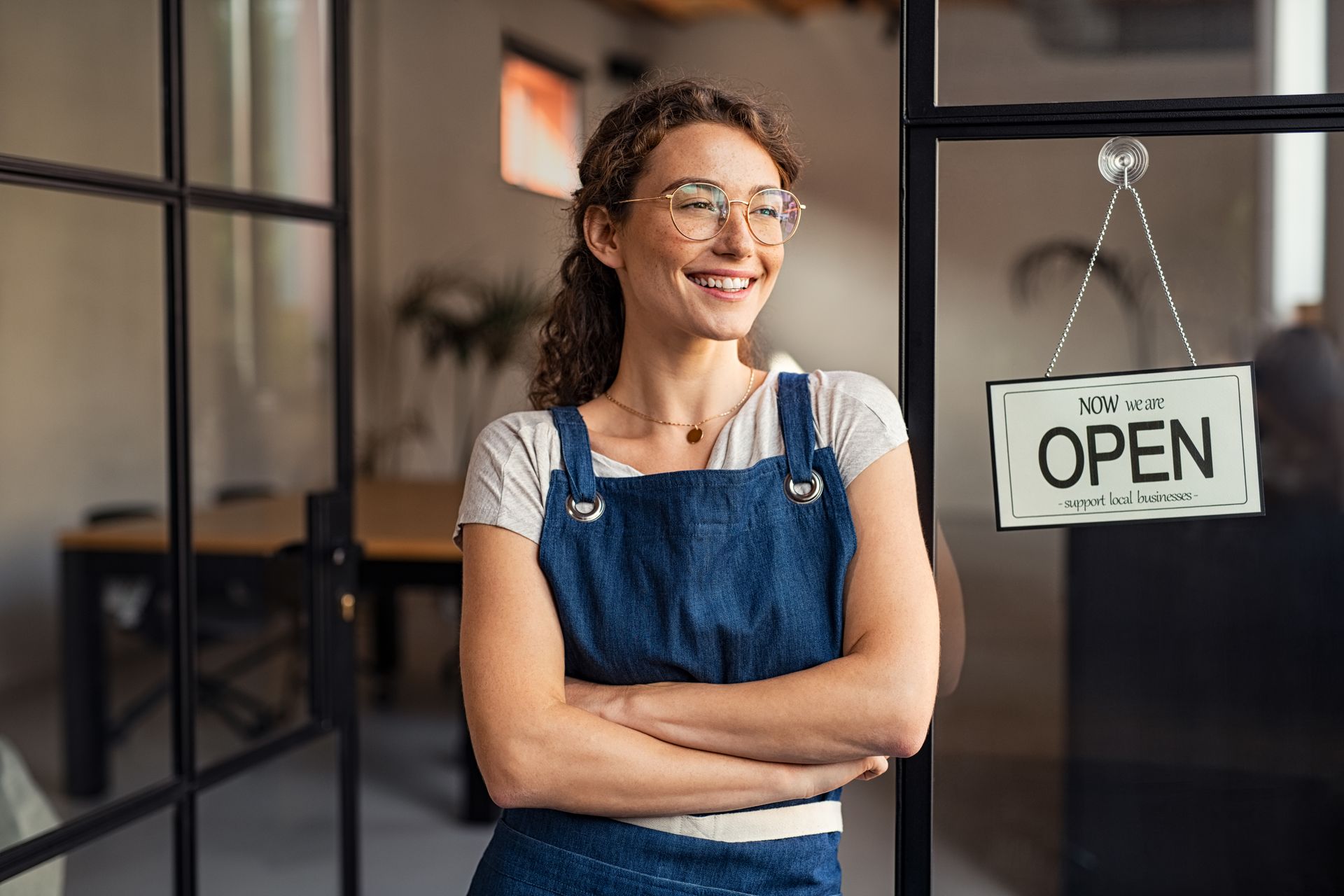 Woman in apron, smiling, arms crossed, stands in doorway with 