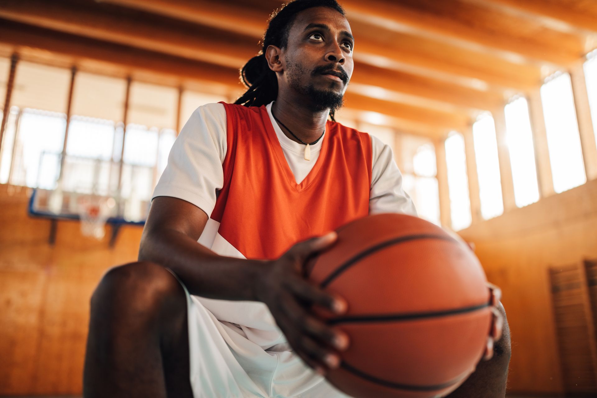 A basketball player is sitting on the floor holding a basketball.