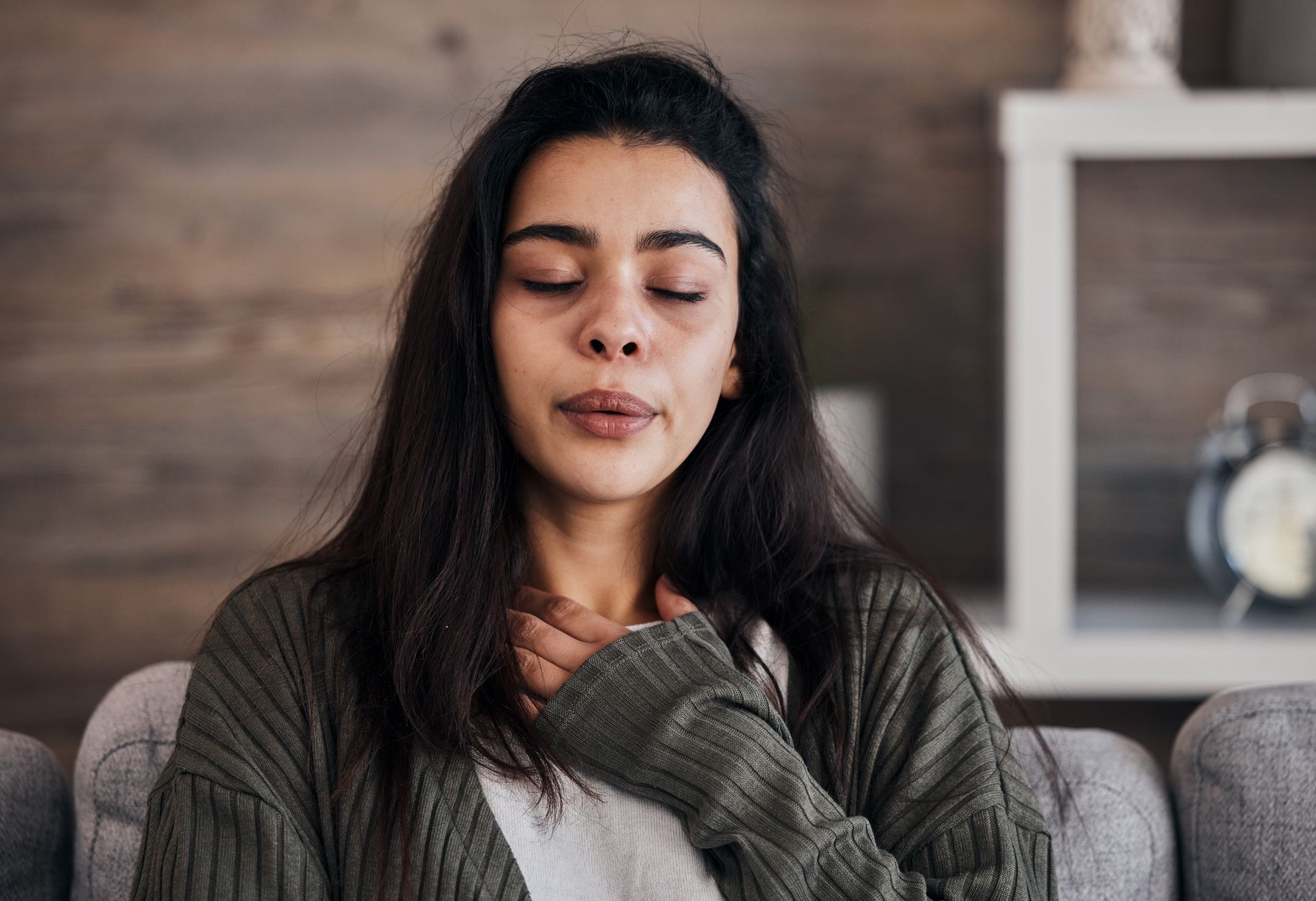 A woman is sitting on a couch with her eyes closed and her hands on her chest.