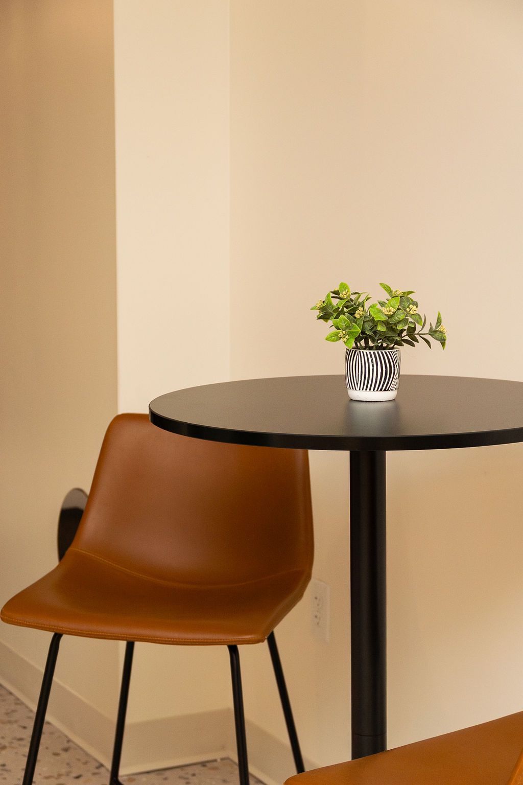 Brown chair beside a round black table with a small potted plant in a minimalist corner