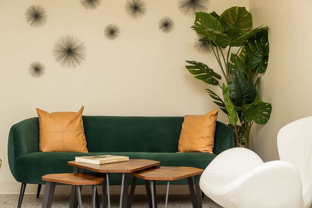 Modern living room with green sofa, mustard pillows, coffee table, white chair, and tall potted plant