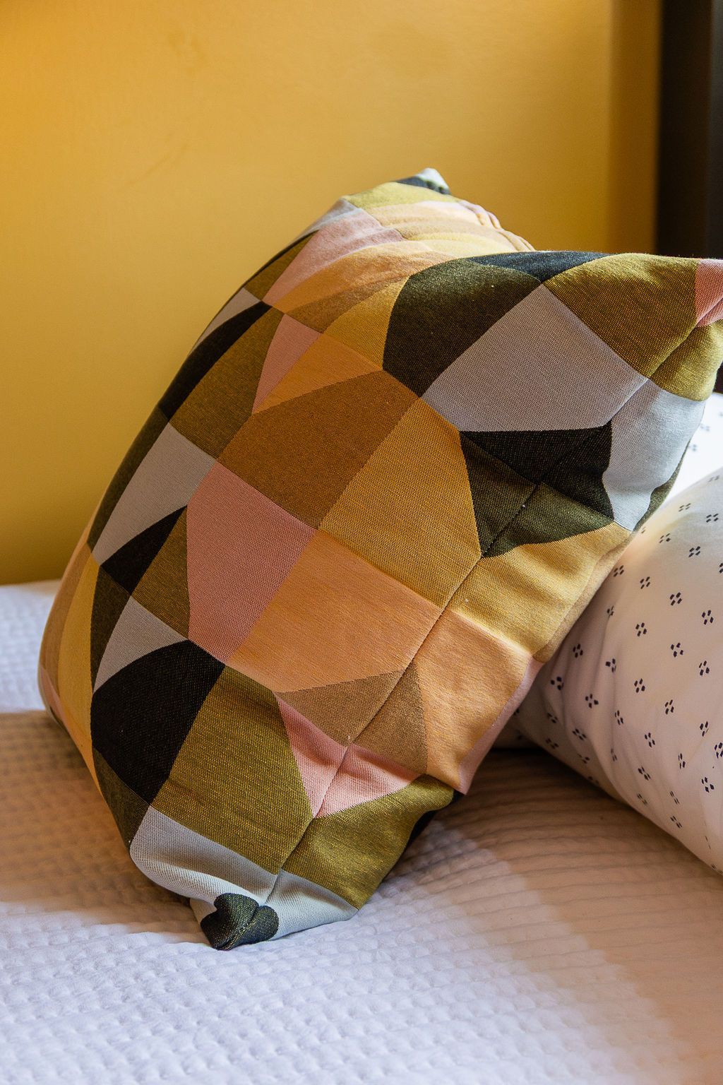 Colorful geometric-patterned pillow on a bed against a yellow wall