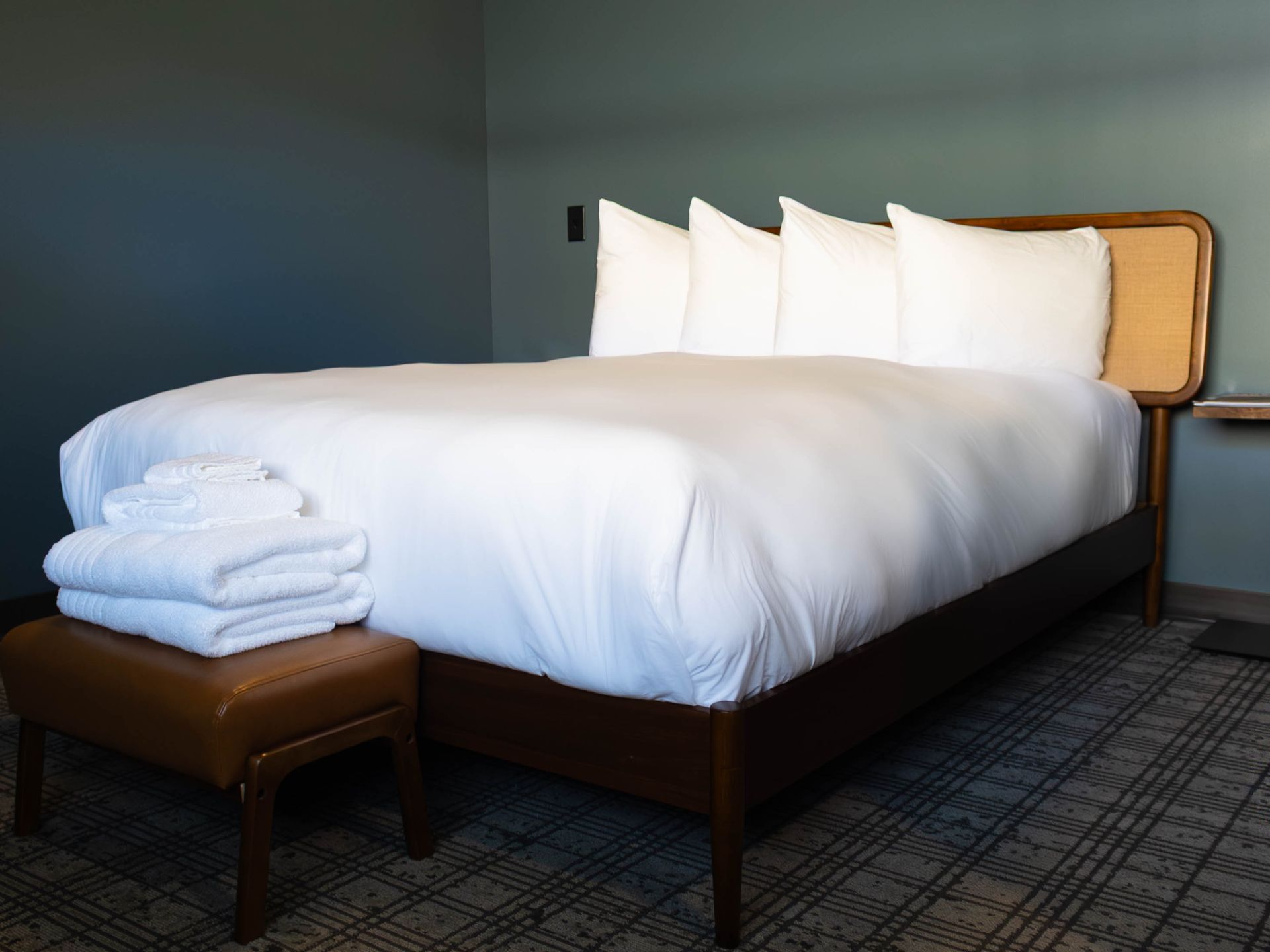 Neatly made bed with white bedding, pillows, folded towels, and a brown bench in a modern room.