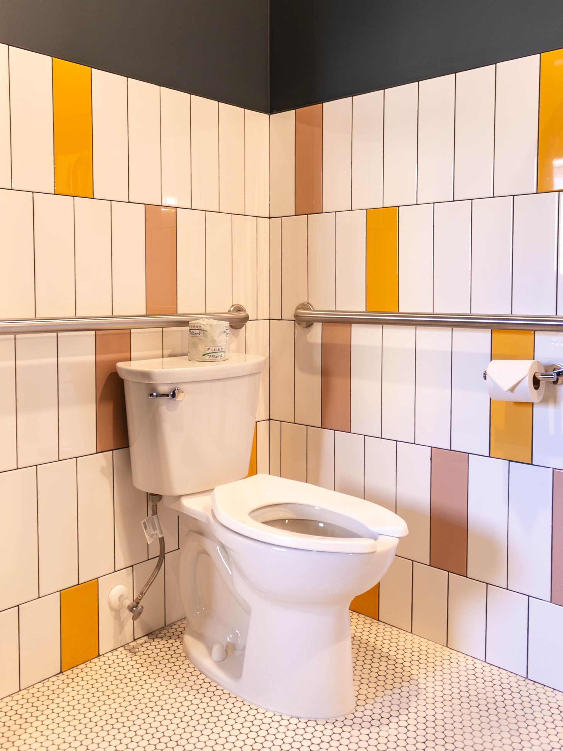 Small bathroom with a toilet, wall-mounted sink, and white-orange striped tile walls.