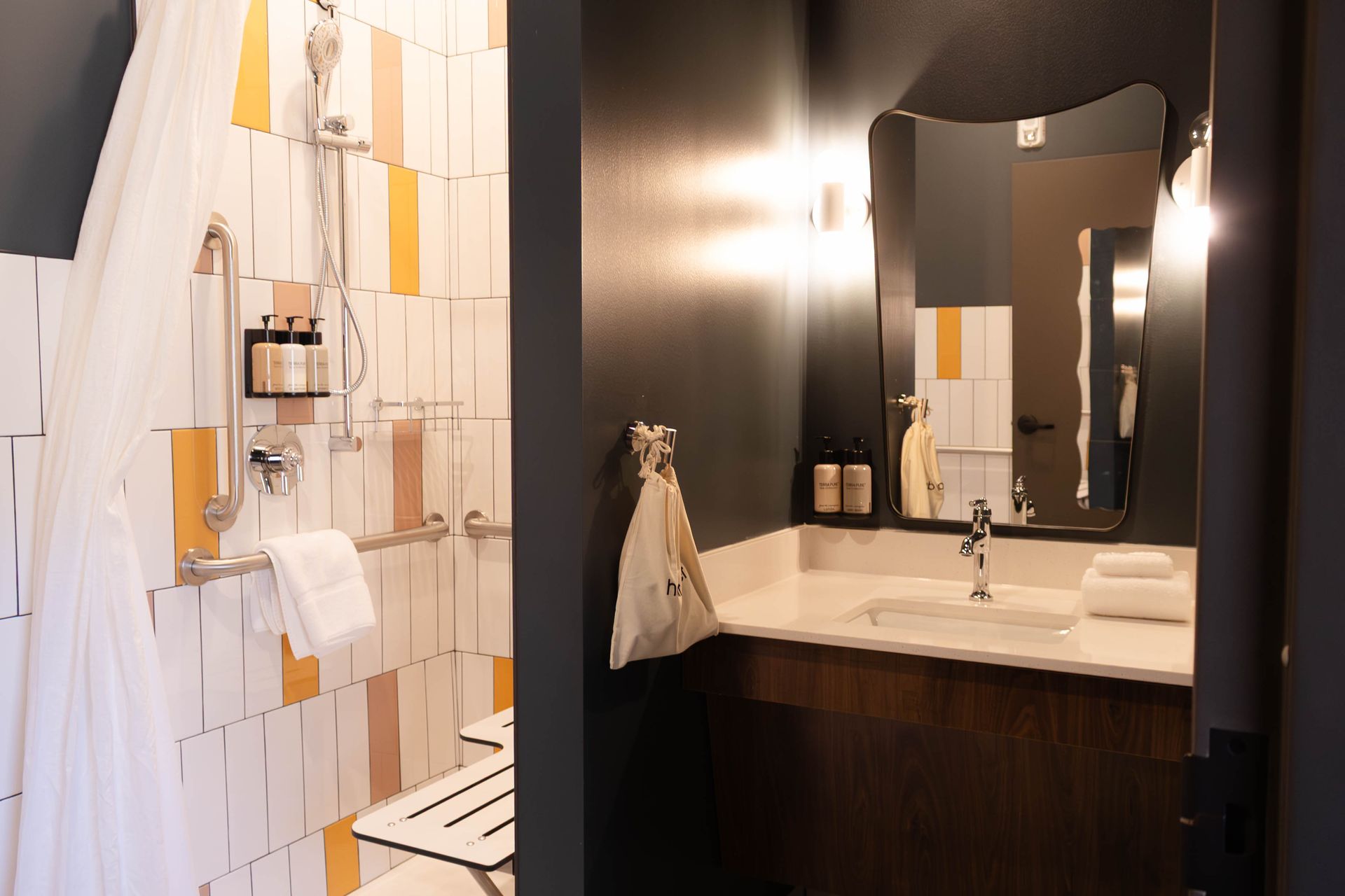 Modern bathroom with dark vanity, white countertop, wall mirror, and hanging towels