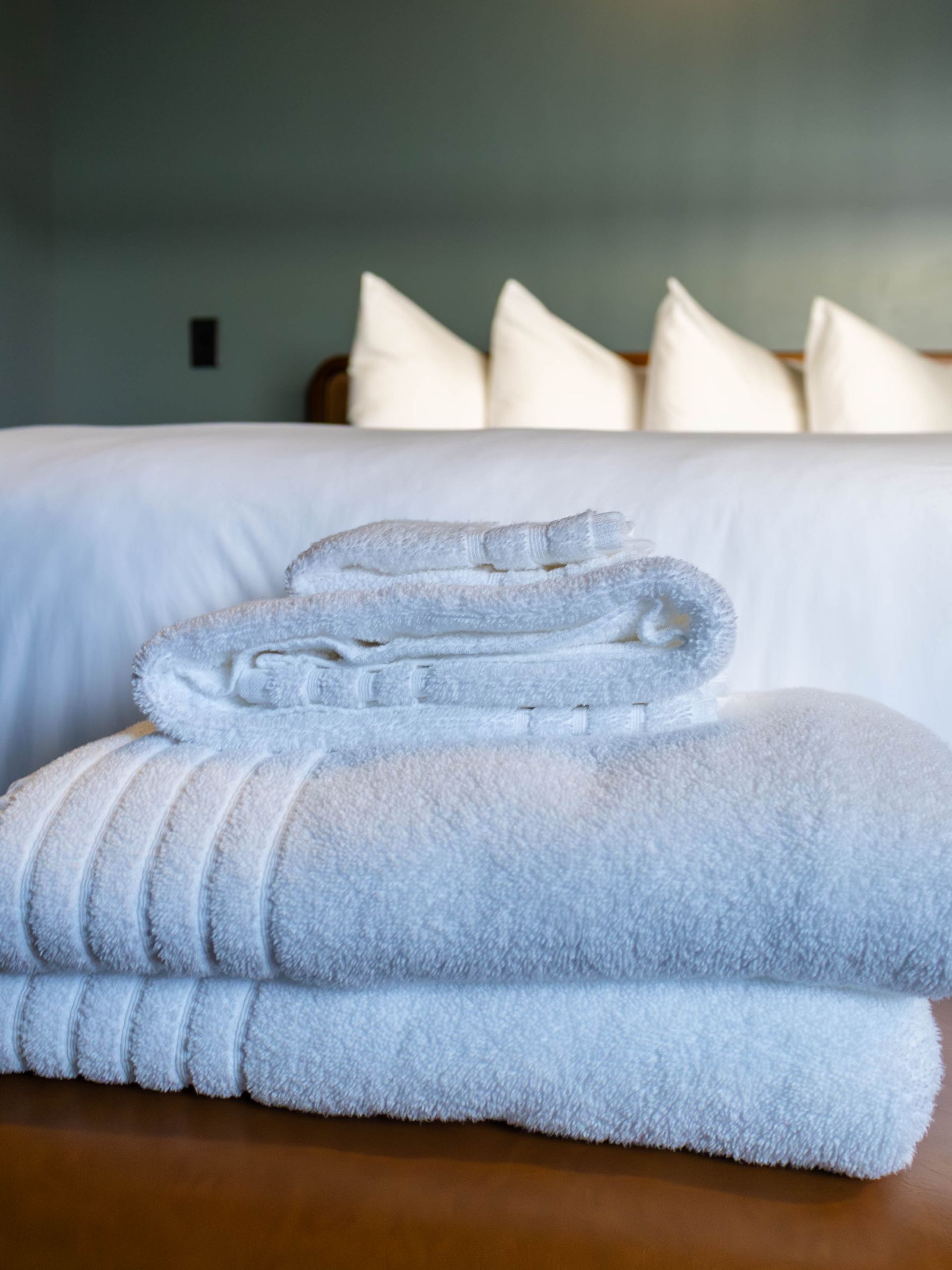 Folded white and light blue towels stacked on a bed in a neat hotel-style room