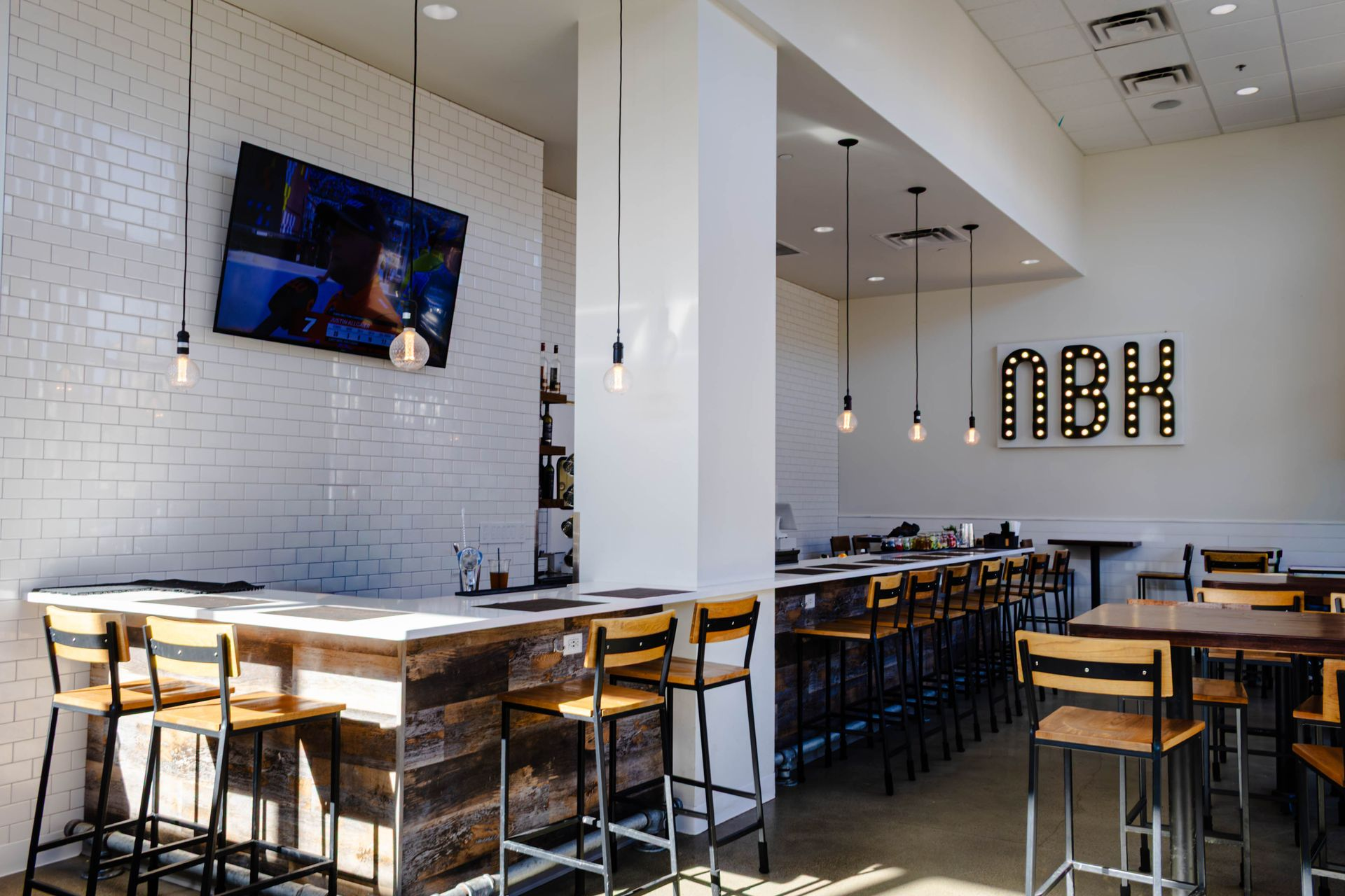 Bright modern restaurant interior with white brick walls, pendant lights, and rows of wooden tables and stools
