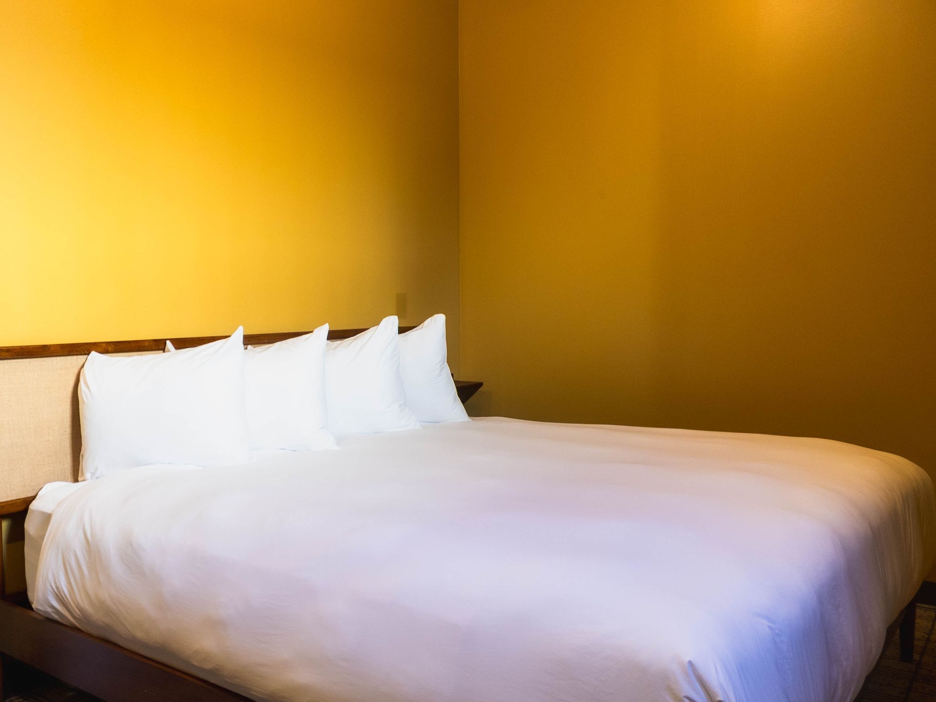 Neatly made bed with white bedding and pillows in a room with warm yellow walls