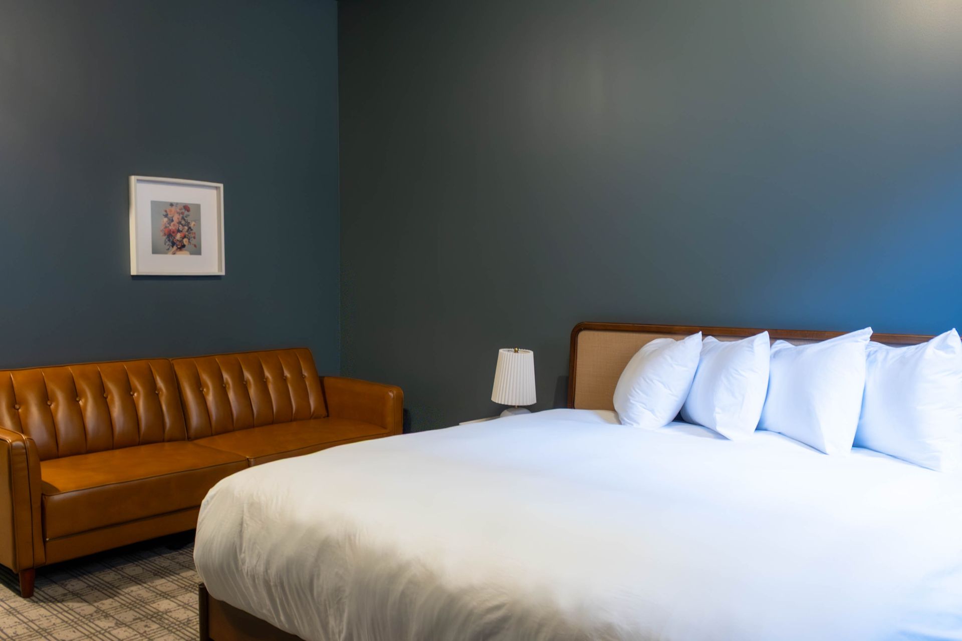 Modern hotel room with a brown sofa, large white bed, and dark blue walls