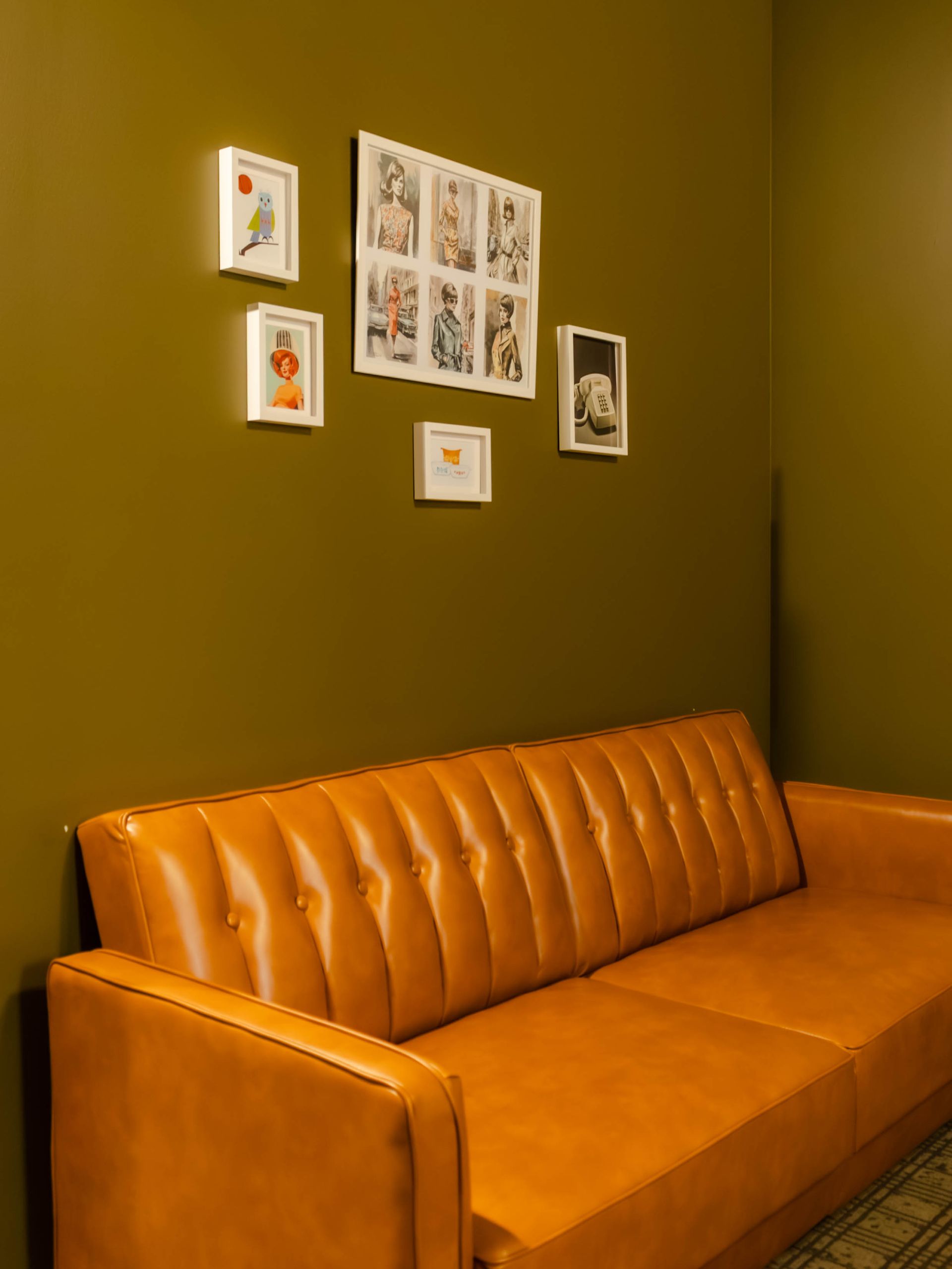 Orange tufted sofa against a green wall with framed art prints above it.