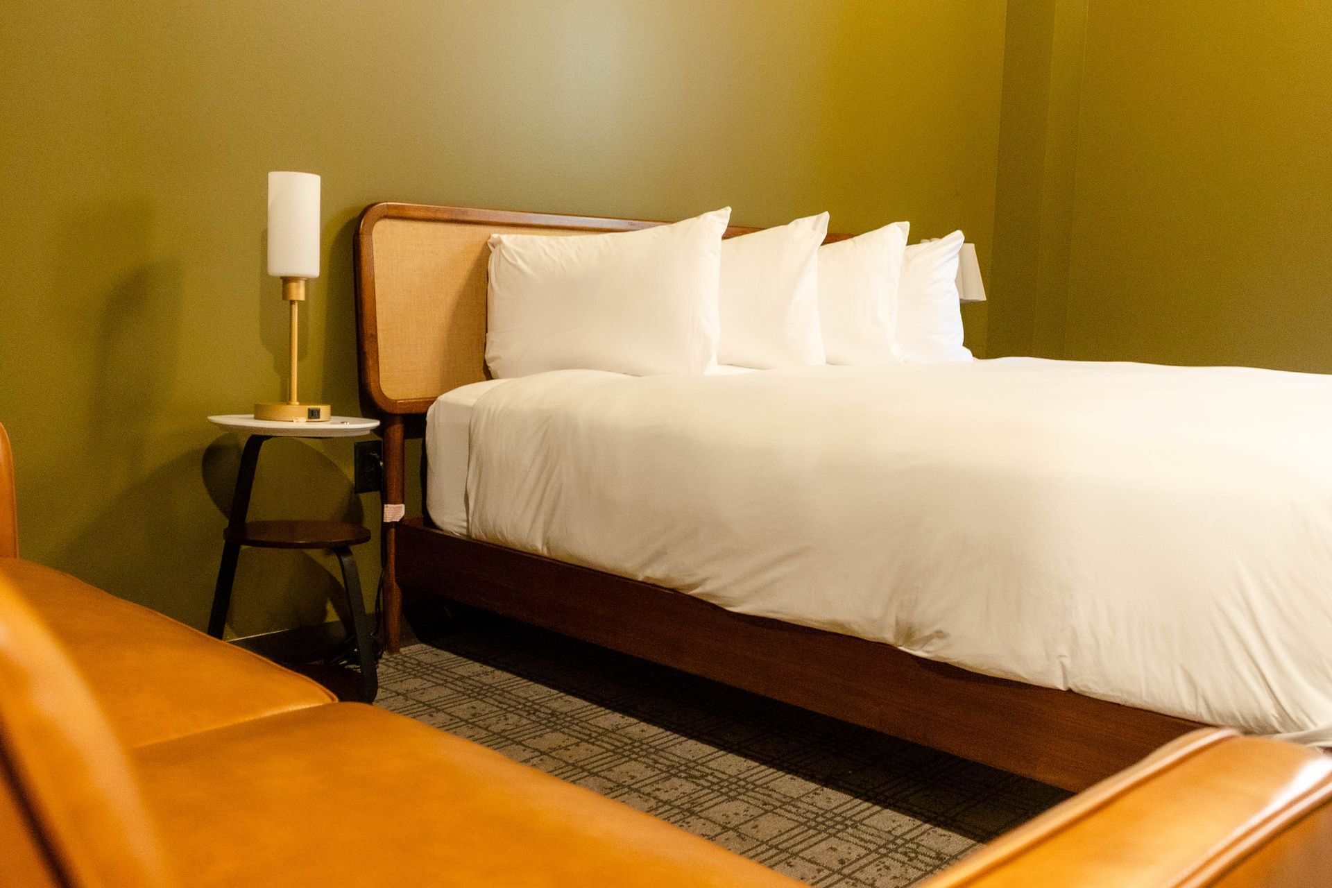Modern bedroom with white bedding, wood bed frame, and orange sofa in a green-walled room