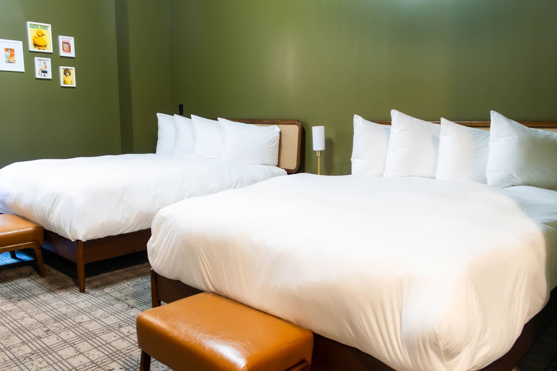 Two white beds in a green-walled hotel room with brown benches and framed wall art.