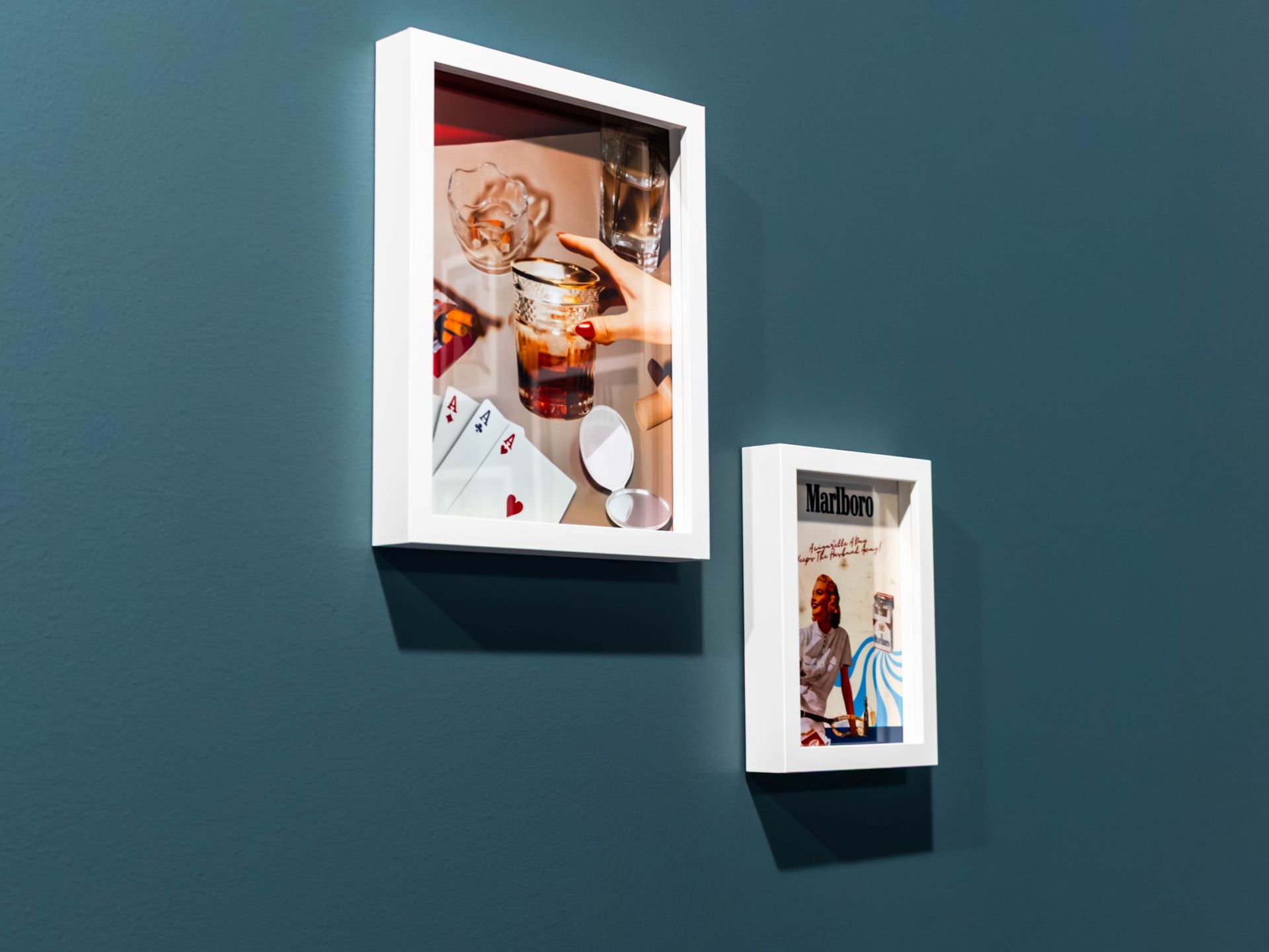Two framed photos on a teal wall, one larger white frame above a smaller frame