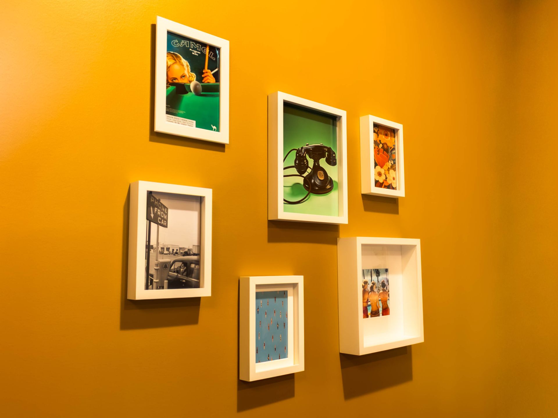 Six framed artworks arranged on a mustard-yellow gallery wall
