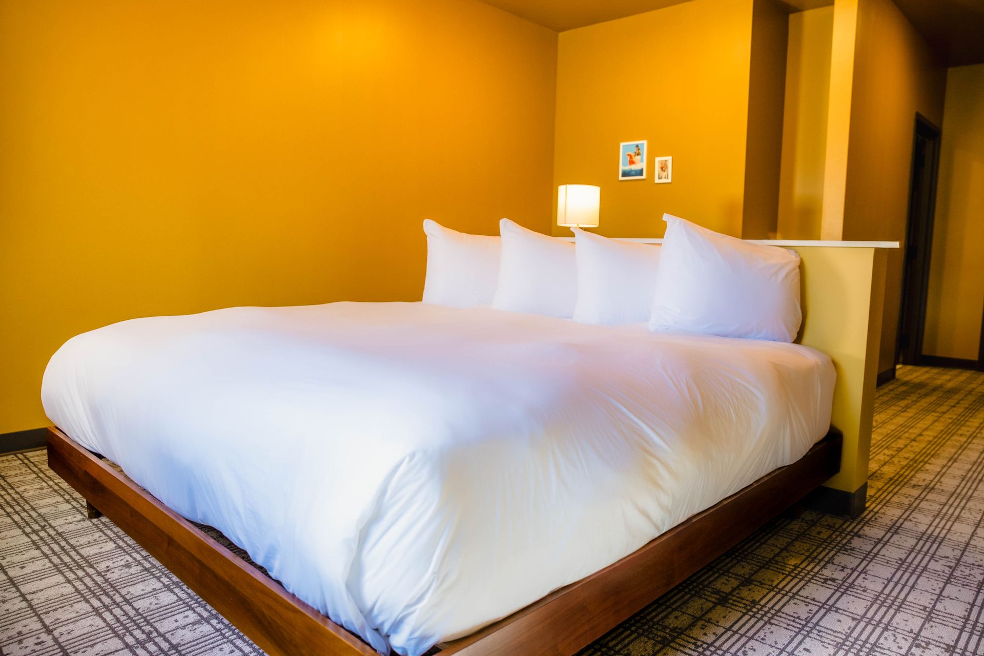 Neatly made white bed in a warm yellow hotel room with carpet and wall art