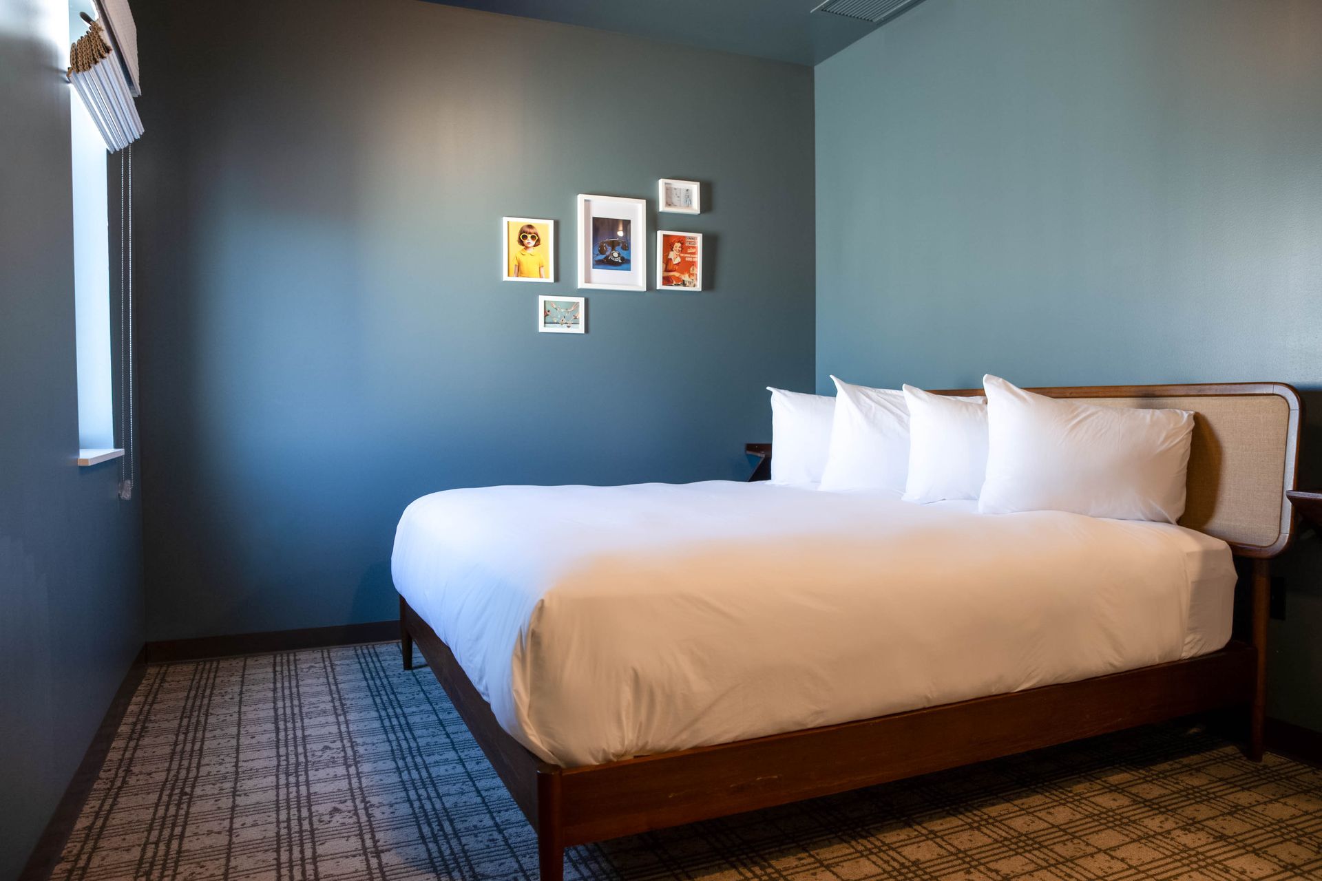 Small bedroom with a made bed, blue walls, framed art, and a patterned rug.