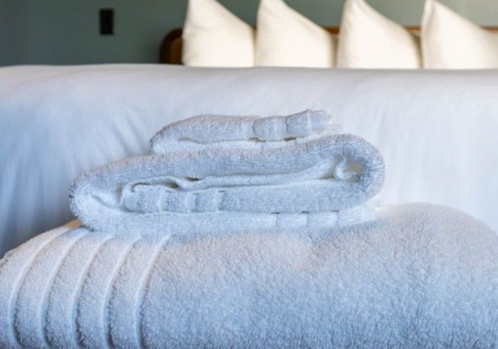 Stacked white towels on a bed in a bright, softly lit room