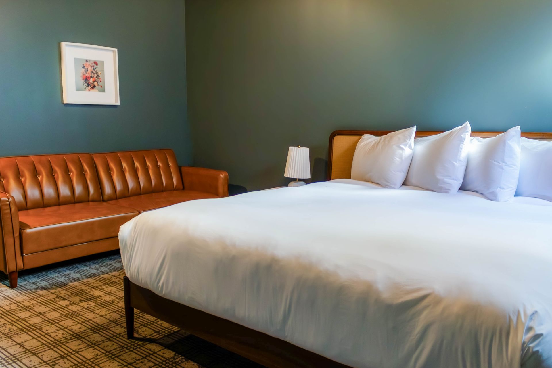 Hotel room with a bed, white pillows, brown leather sofa, and framed wall art