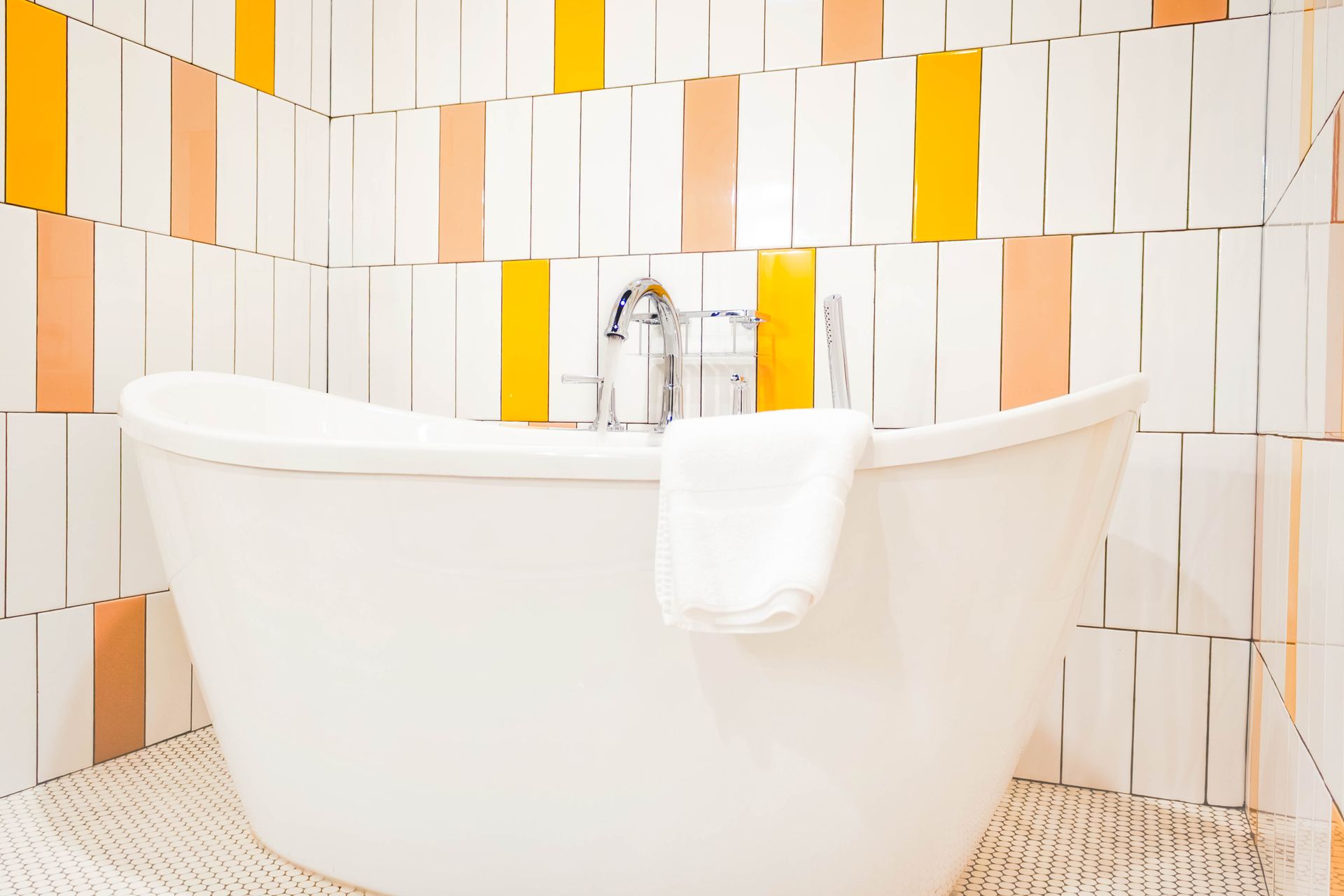White bathtub with a towel, set against a patterned white and yellow tiled wall.