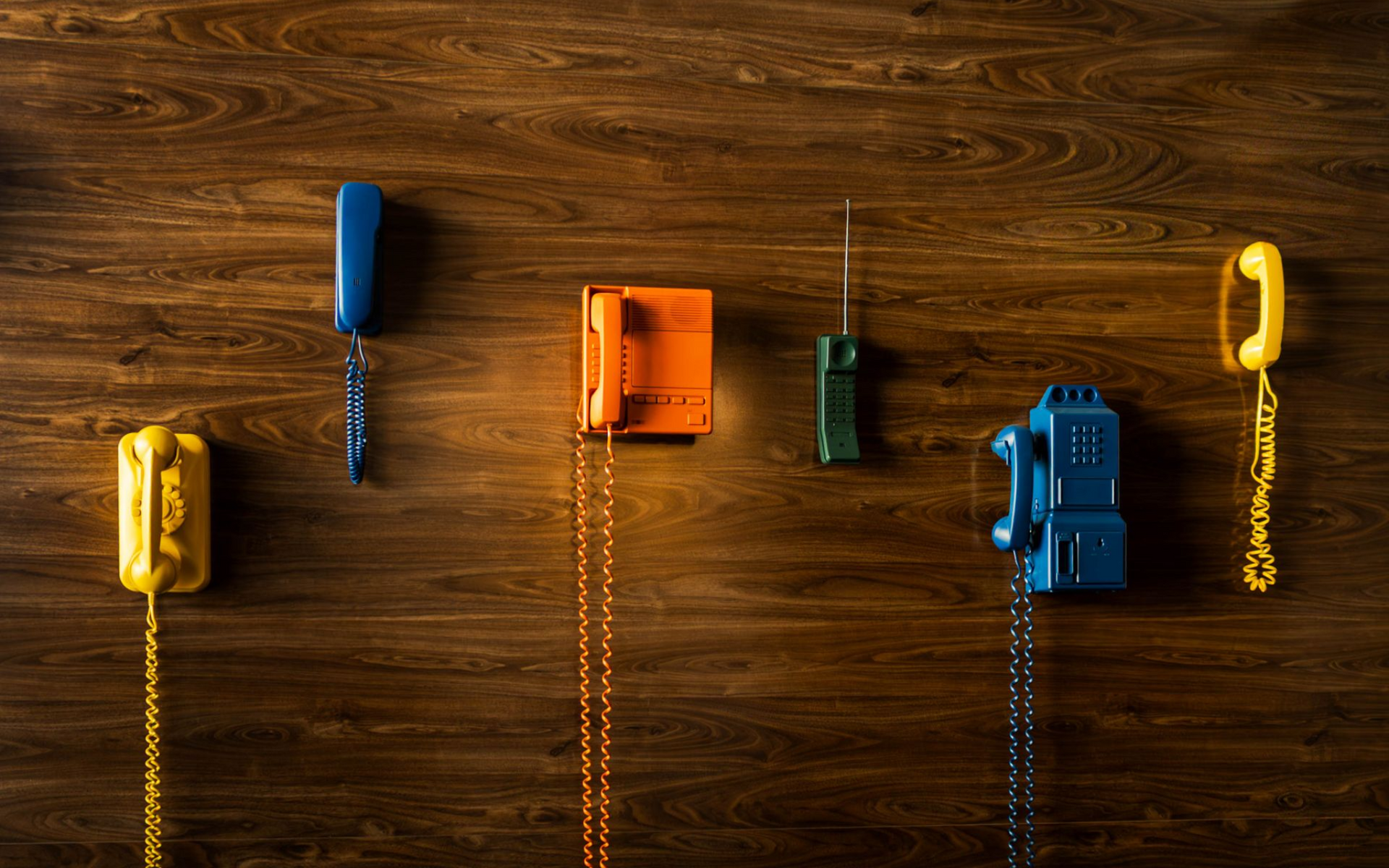 Colorful miniature tools lined across a wooden surface: wrench, screwdriver, block, clamp, drill, and key.