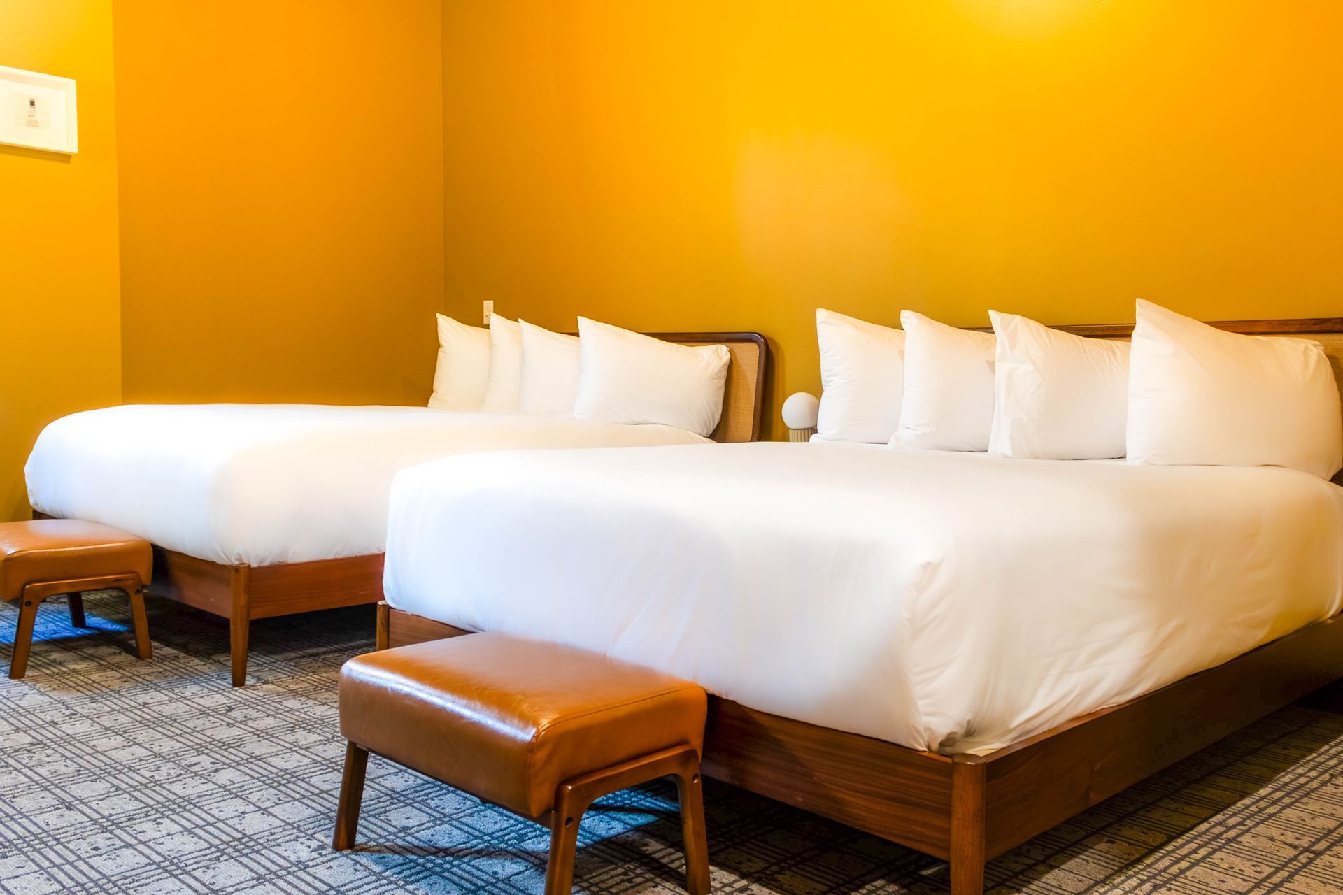 Two neatly made white beds with brown benches in a bright yellow hotel room