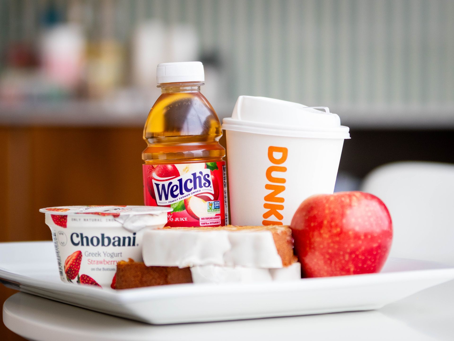 Breakfast tray with yogurt, egg, apple, juice, and a Dunkin' cup