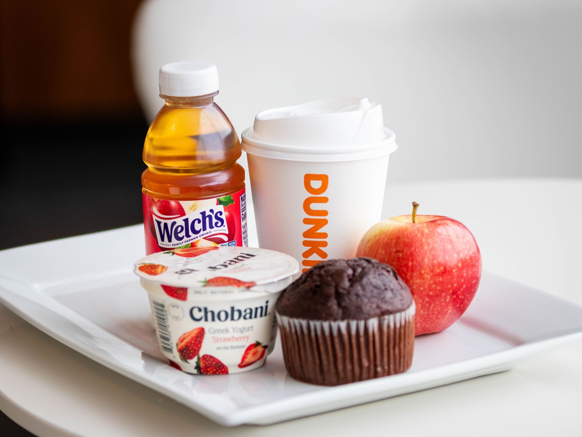 Welch’s juice, Dunkin’ coffee, yogurt, muffin, and apple on a white tray