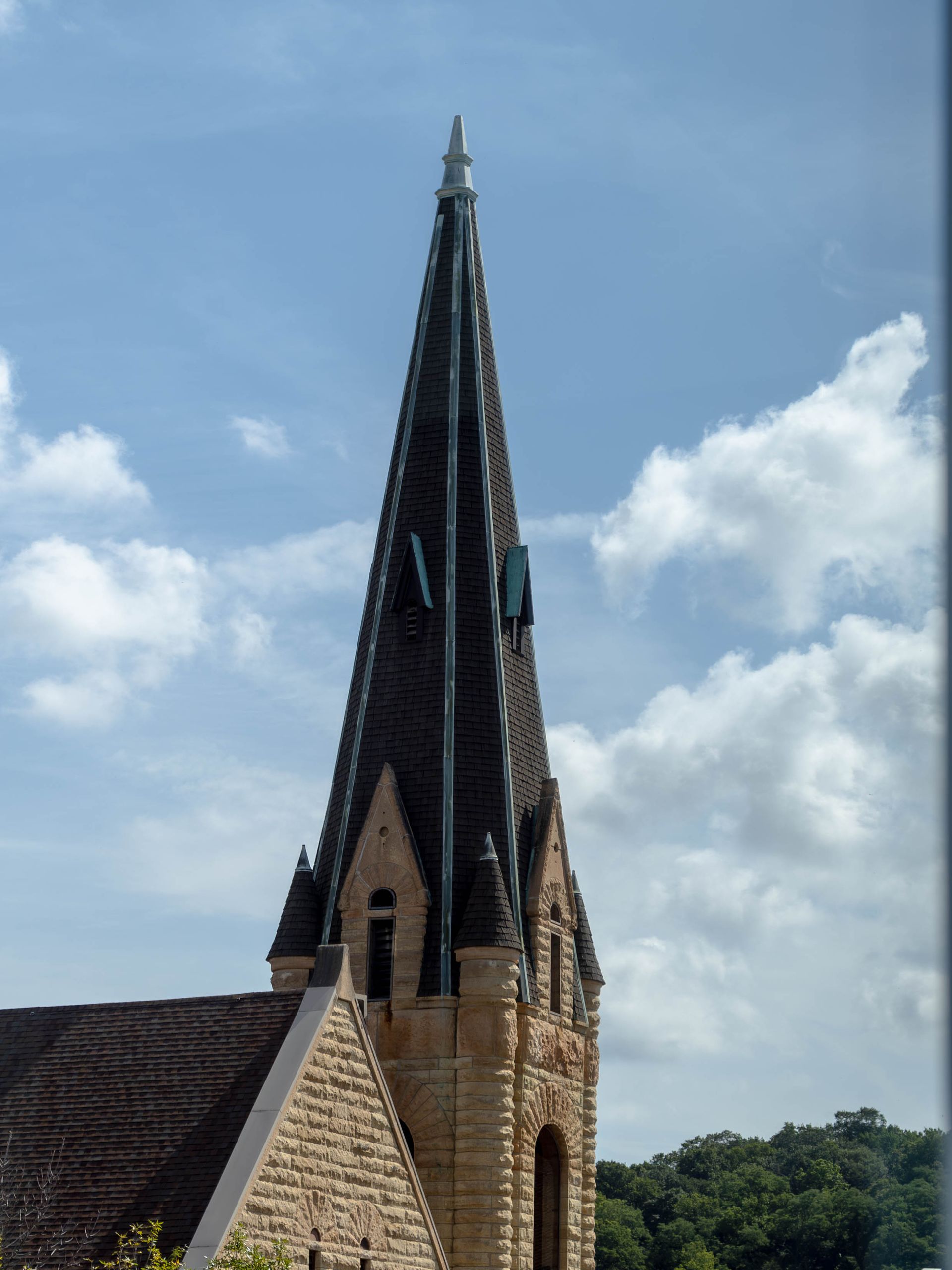 Stone church steeple with a dark spire against a blue sky and clouds