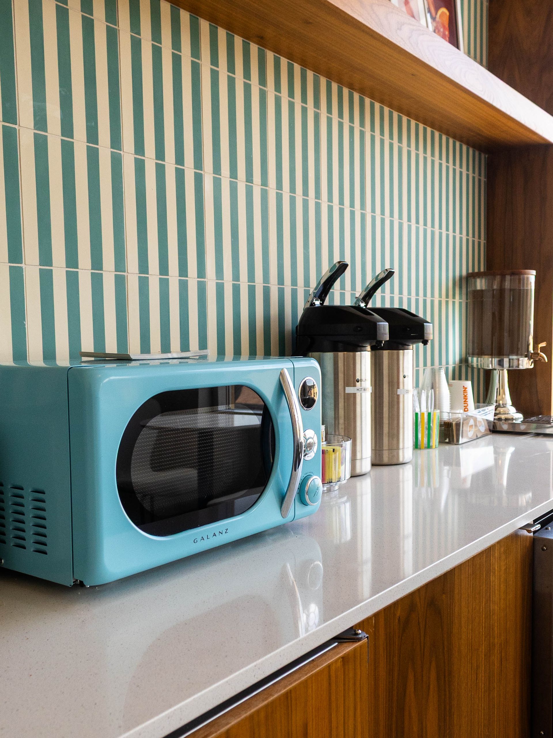 Turquoise toaster oven on a white kitchen counter beside two coffee grinders and a glass jar