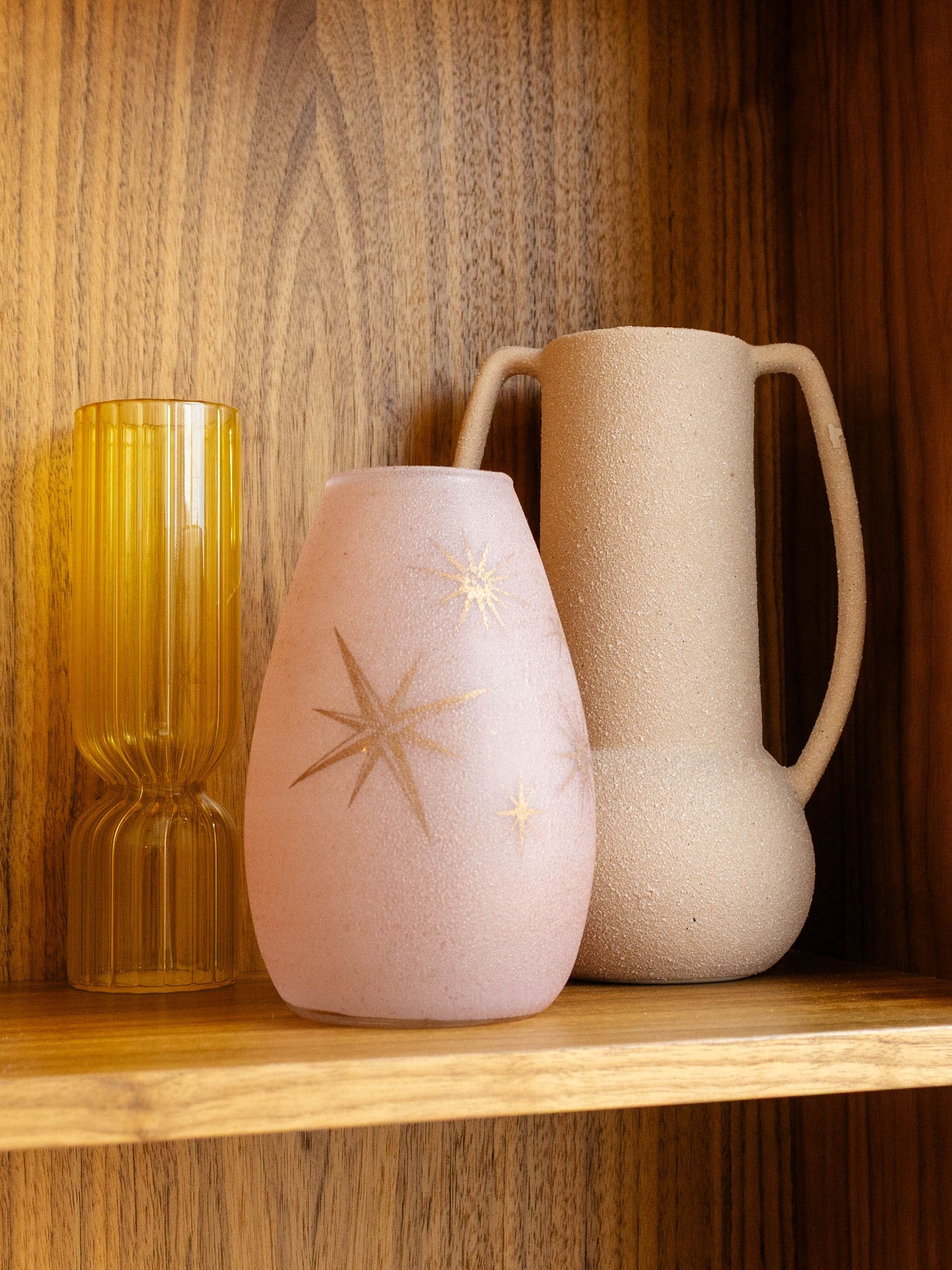 Three decorative ceramic vases on a wooden shelf against a wood-paneled background