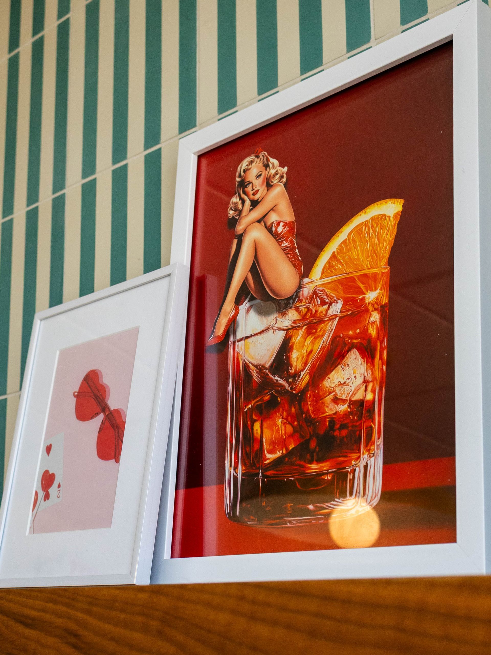 Framed red-toned poster on a striped wall beside a smaller floral print