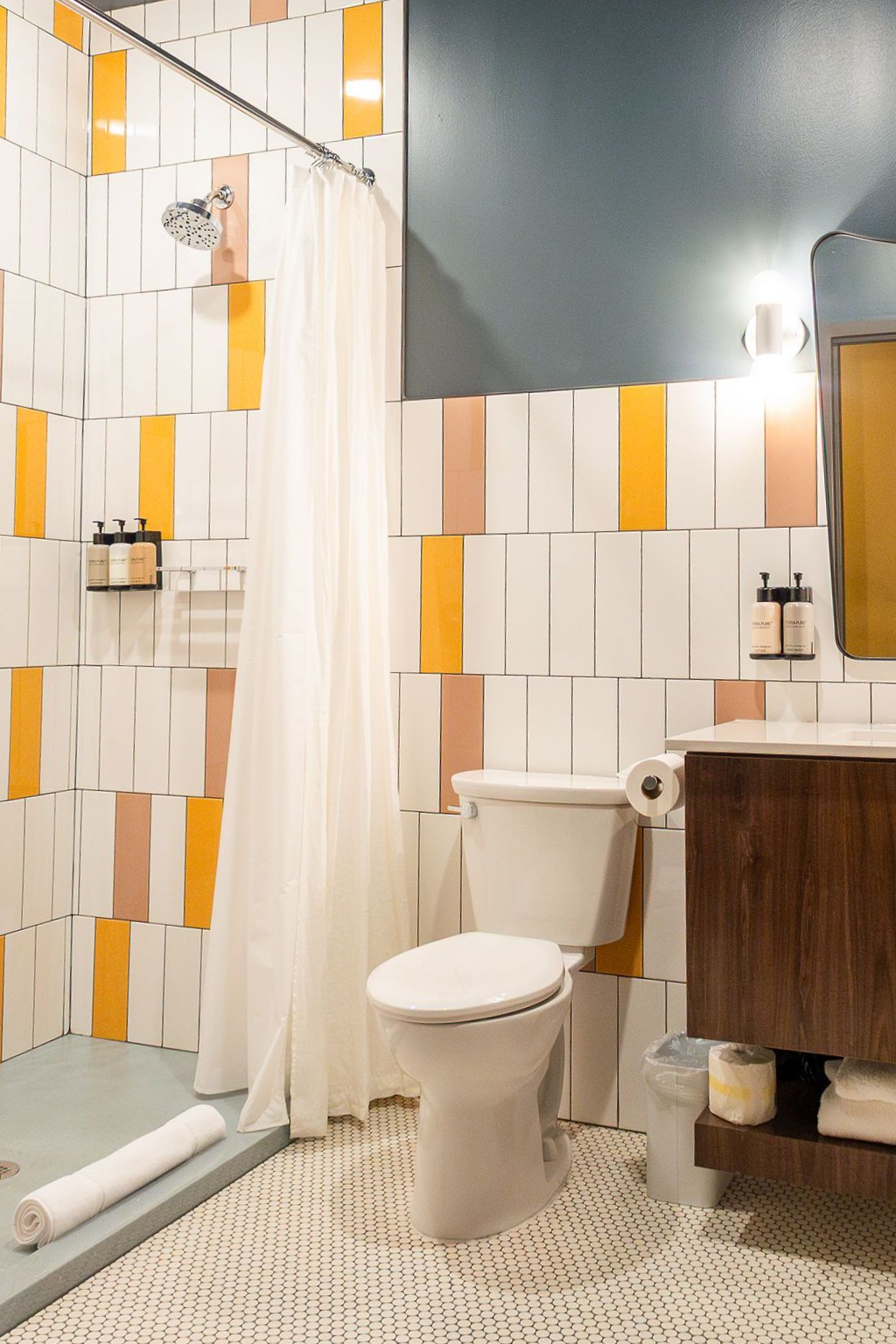Modern bathroom with white and orange tiled walls, shower curtain, toilet, sink, and wood vanity.