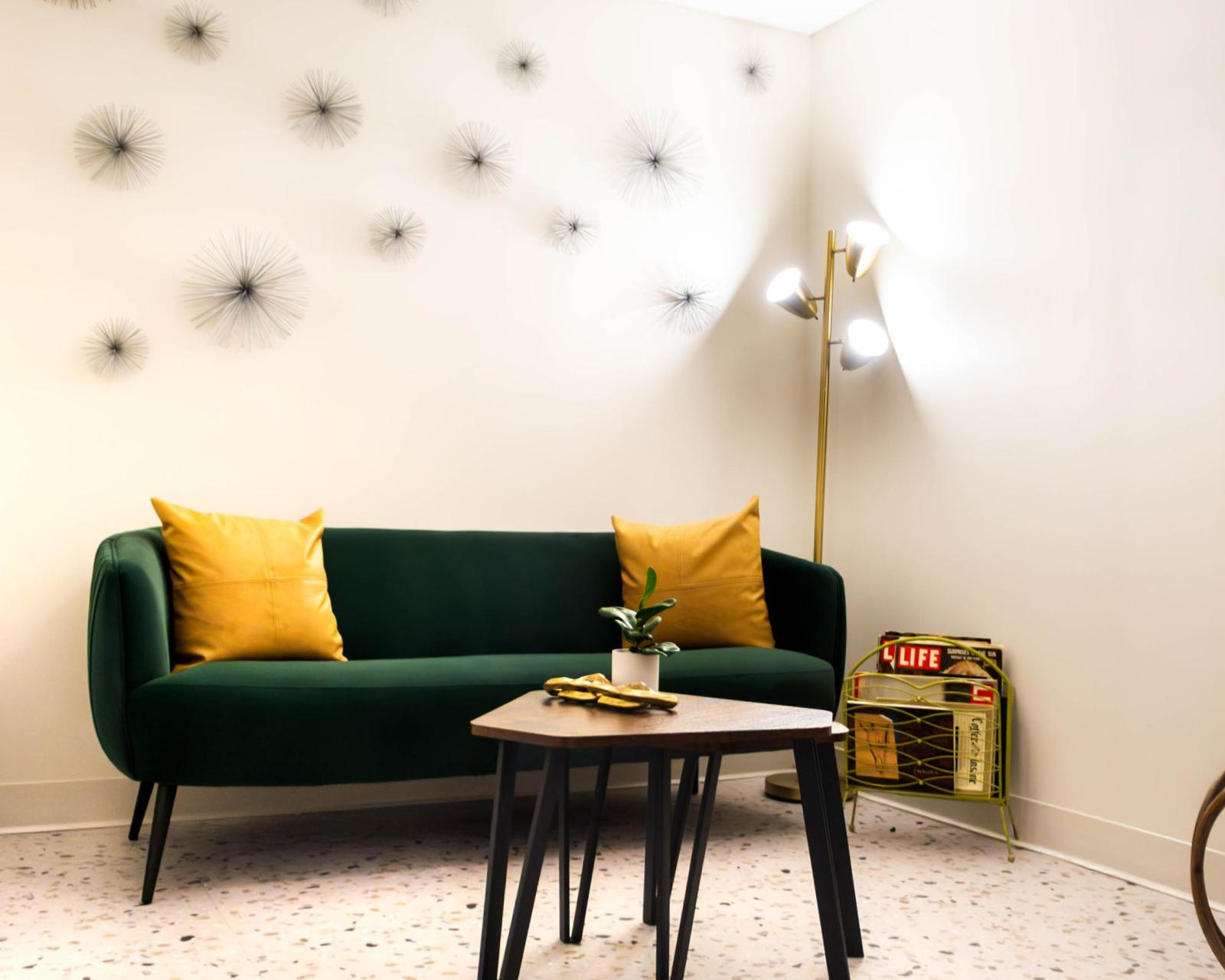 Green sofa with yellow pillows in a bright room, beside a floor lamp and small coffee table.