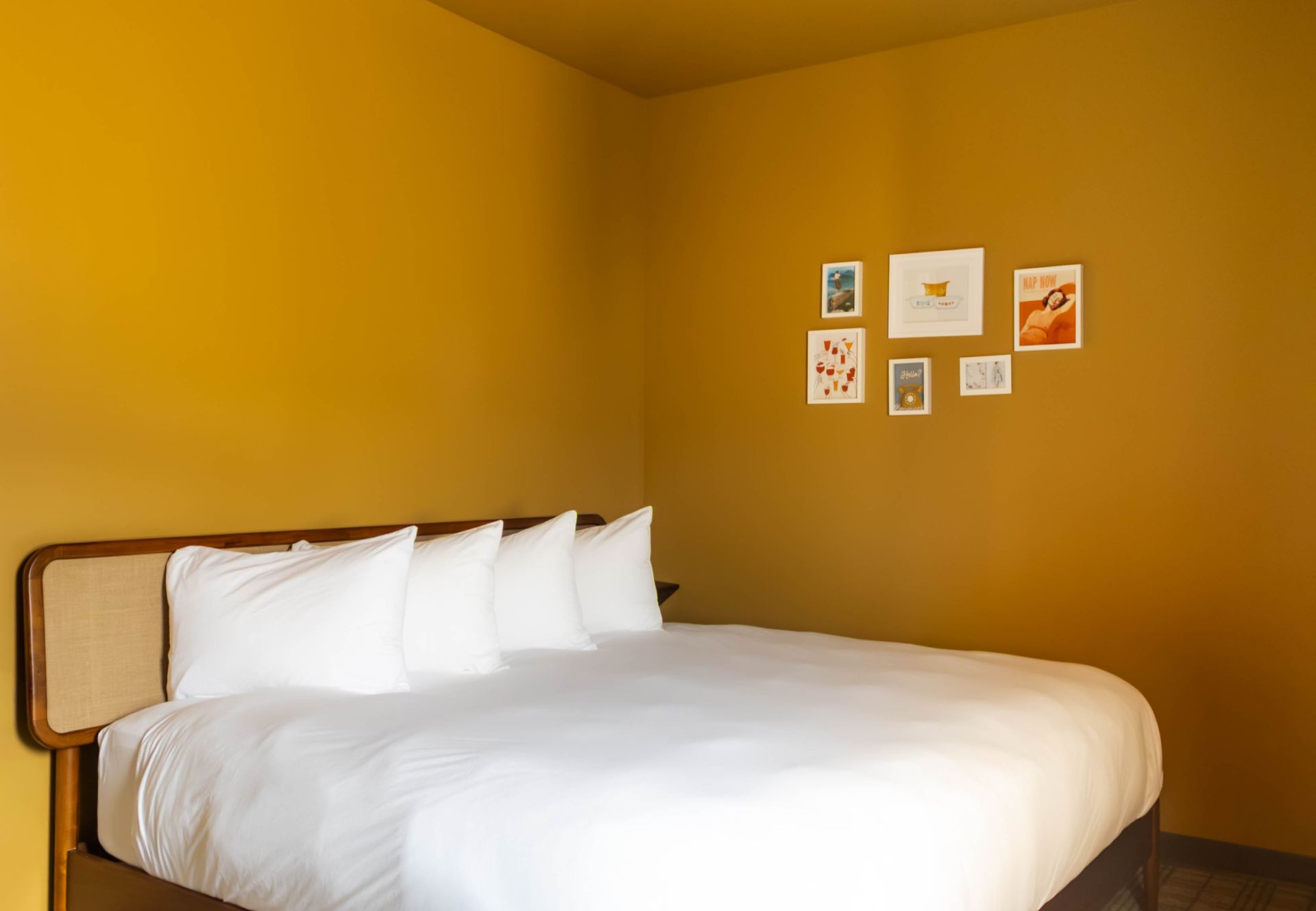 Minimal bedroom with mustard-yellow walls, white bed linens, and small framed art above the bed