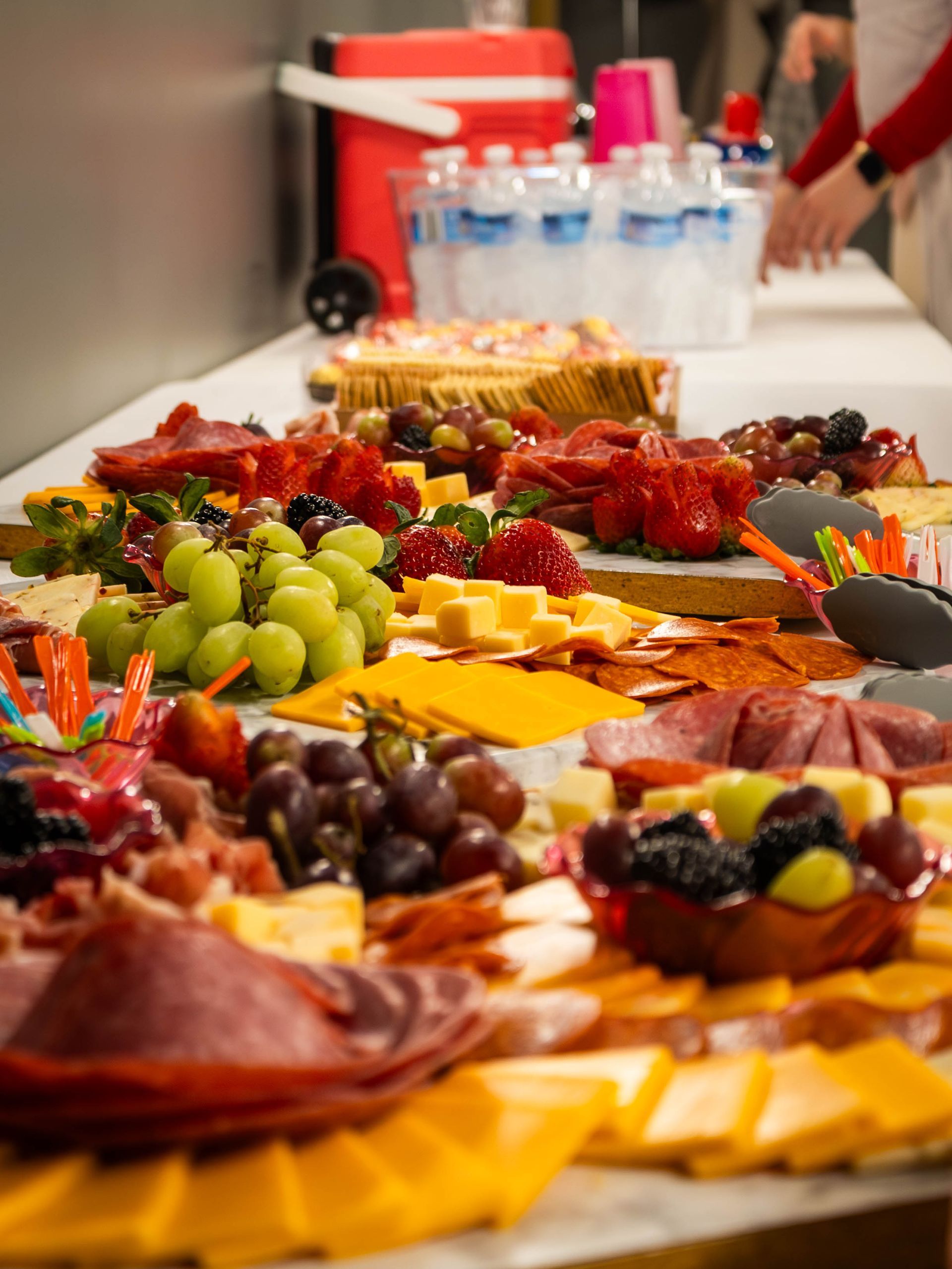 Charcuterie and cheese platters with grapes and berries on a buffet table, with bottled water in the background