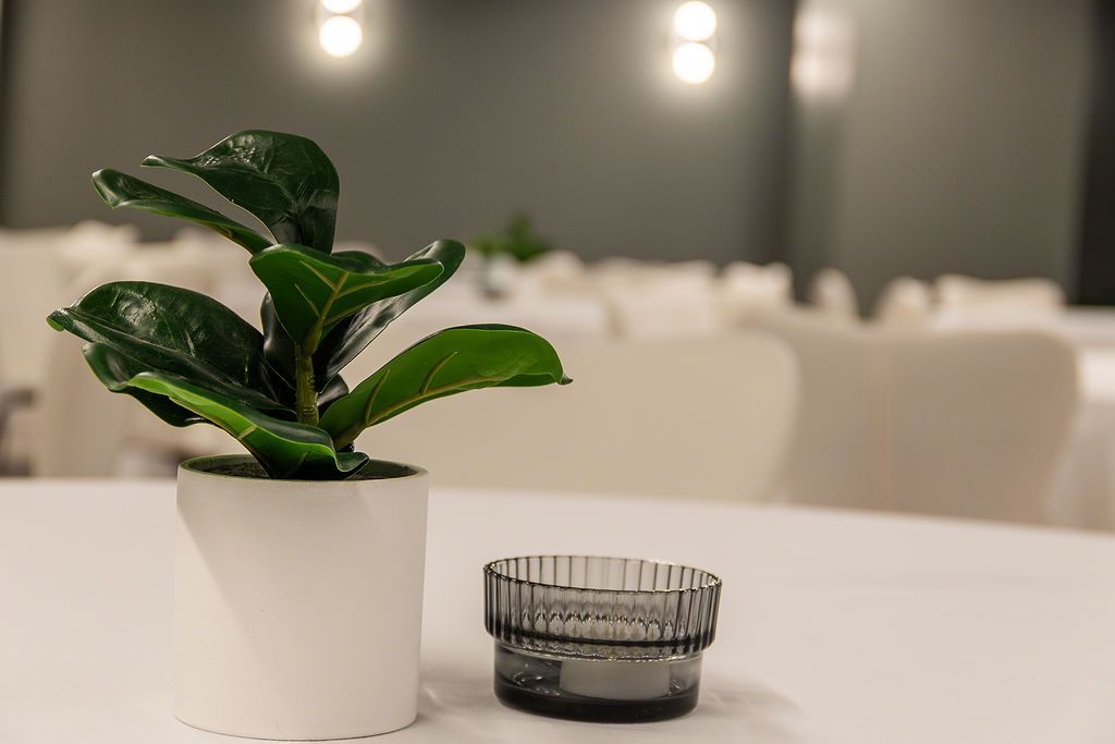 Small potted plant and glass candle holder on a white table in a softly lit banquet room
