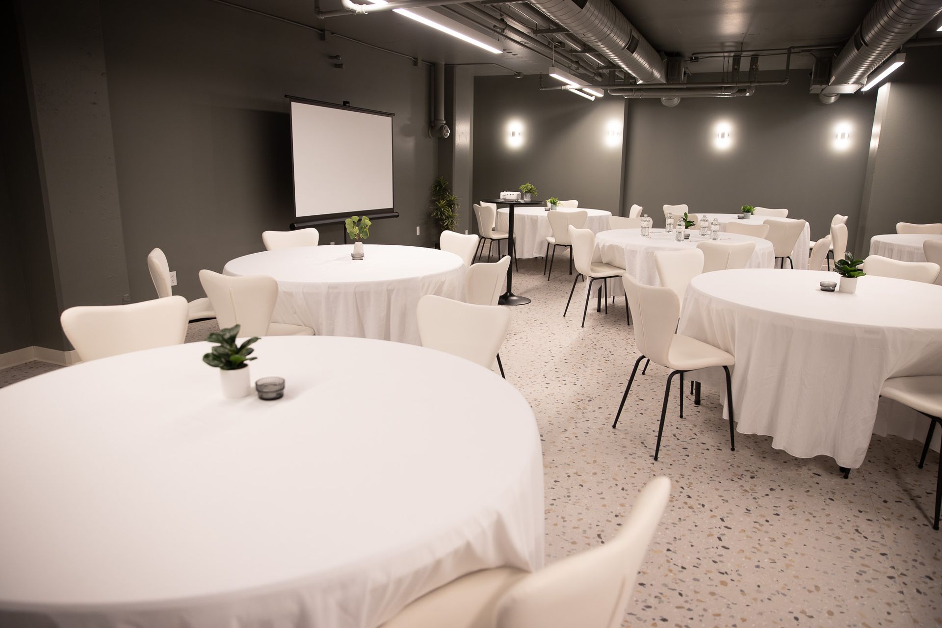 Empty banquet room with round white-clothed tables and white chairs under dim lighting