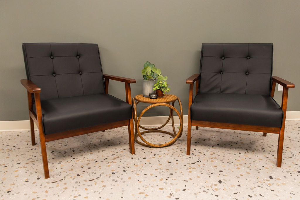 Two black armchairs with wooden arms flank a small round table holding a potted plant.