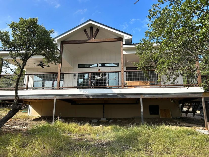 A large house with a large deck is sitting in the middle of a grassy field.