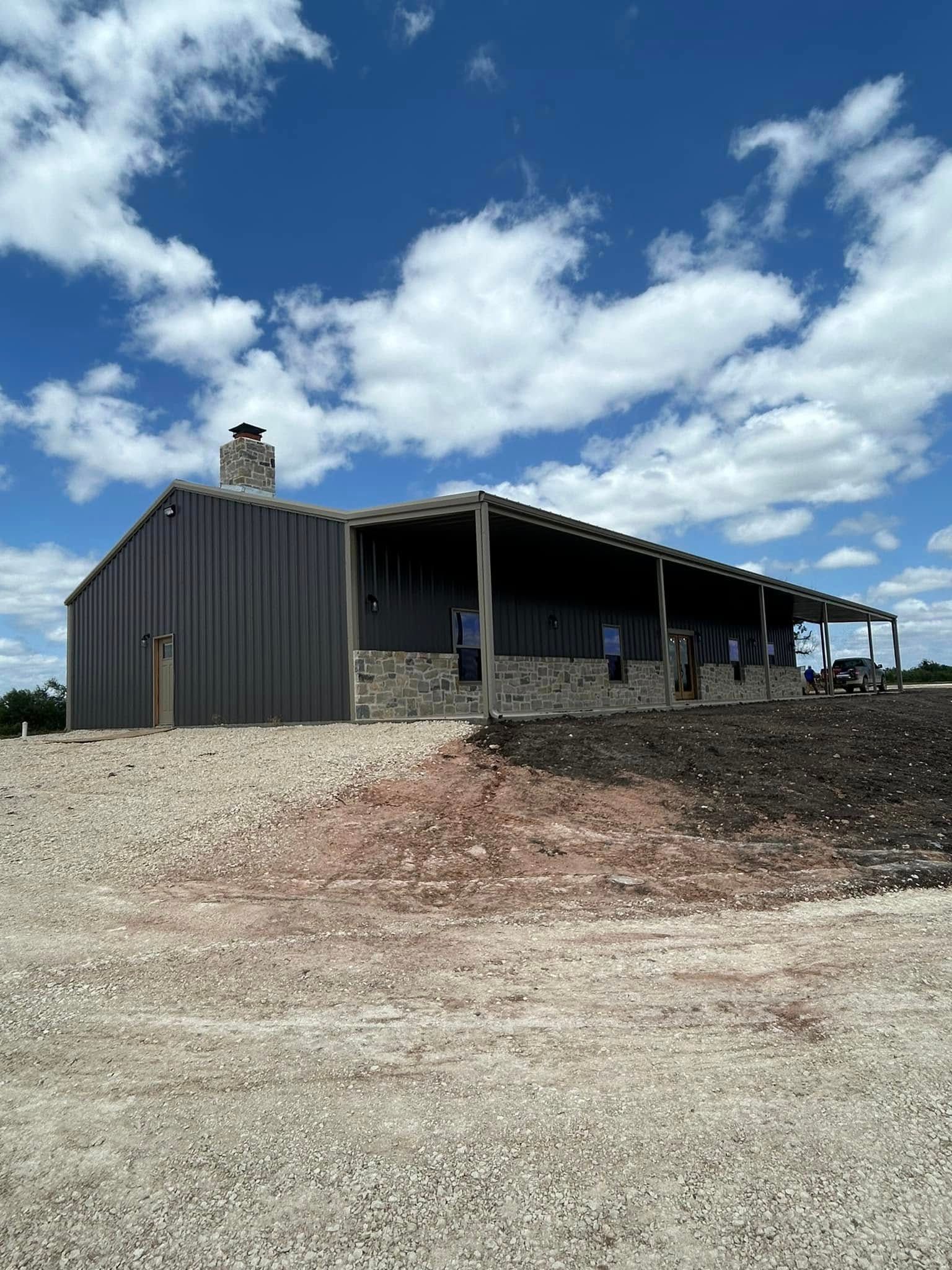 A large metal building with a porch is sitting on top of a dirt field.
