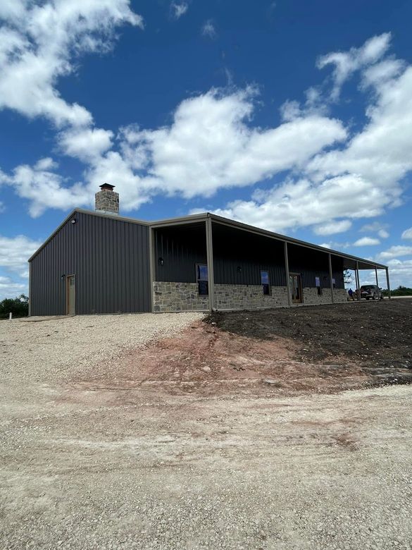 A large metal building with a porch is sitting on top of a dirt field.
