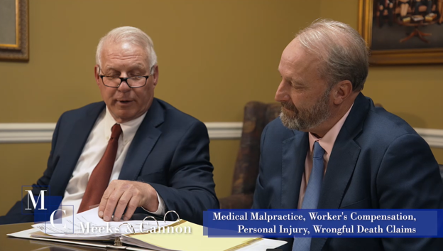 Two men in suits review documents at a conference table in a meeting room.