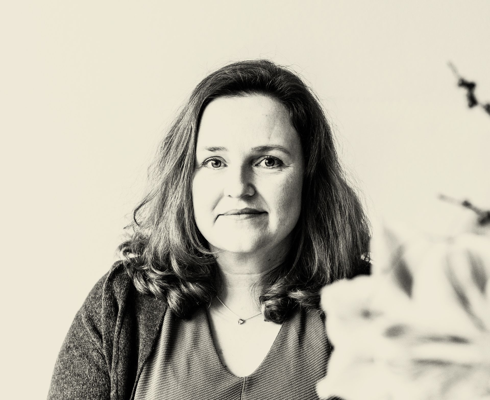 Vrouw met lang haar, gekleed in een trui, kijkt recht in de camera, zachte belichting.